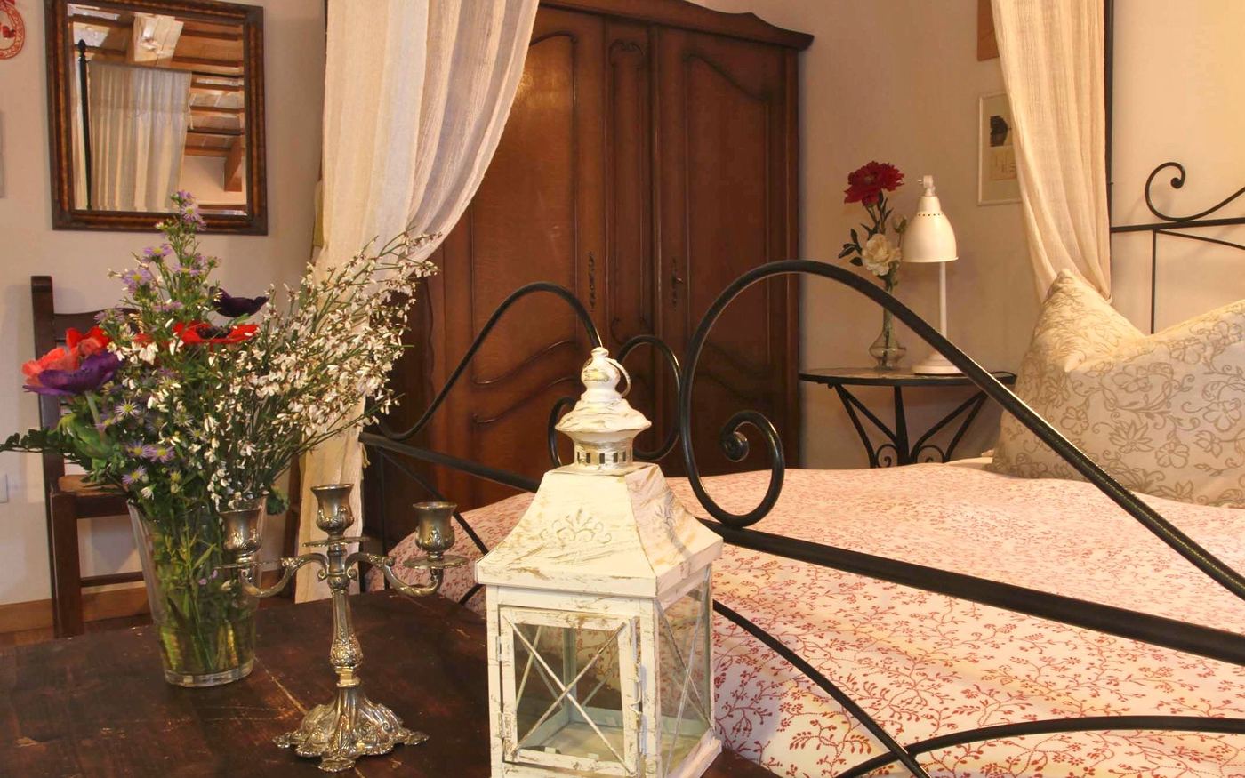 Camera con letto in ferro, fiori freschi e lanterna