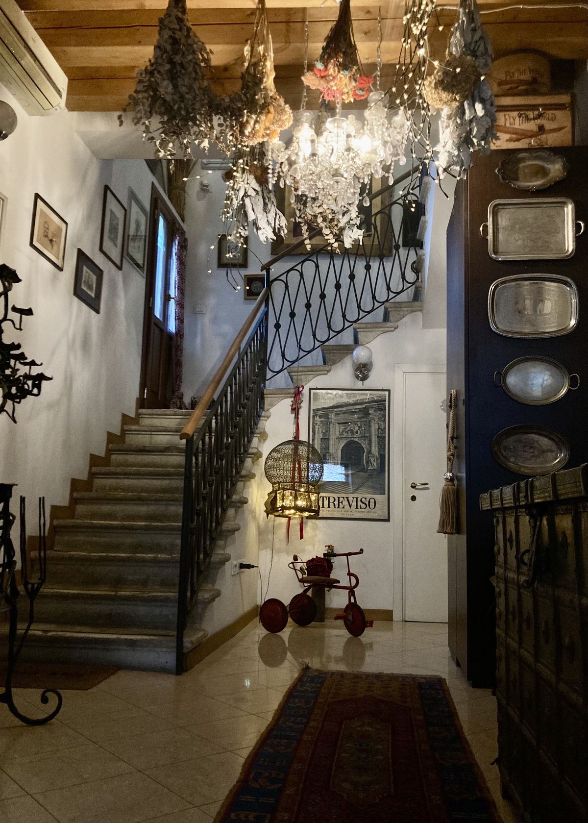 Ingresso con scala in ferro battuto, lampadario e fiori secchi appesi